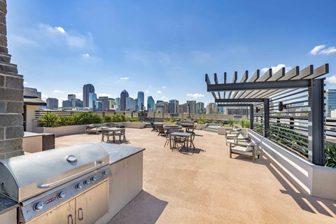 A rooftop patio with a grill and chairs overlooking a city skyline.