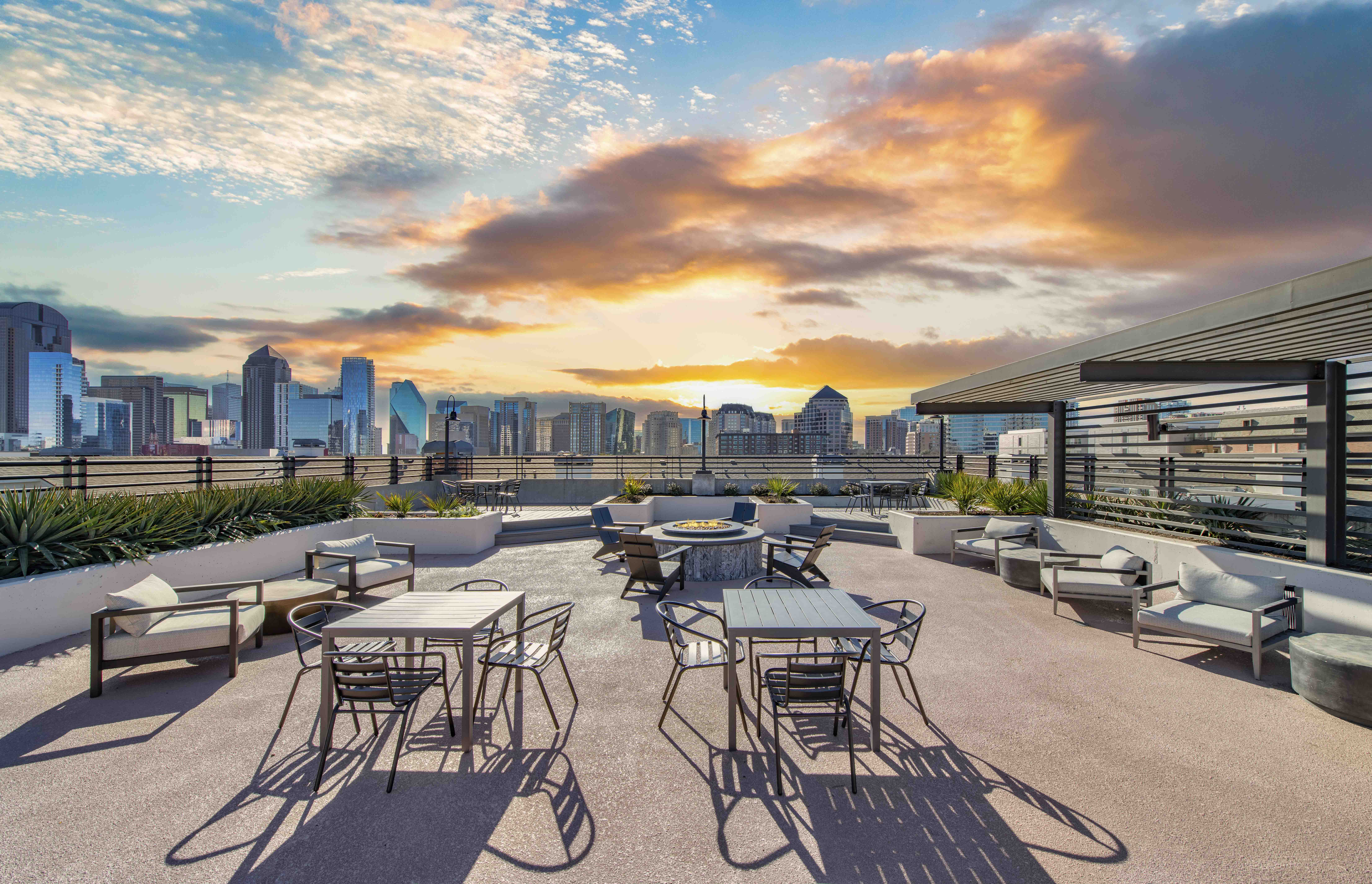 a rooftop patio with tables and chairs and a city skyline at sunset