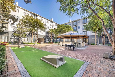 A small gazebo is surrounded by a brick patio and a green lawn.
