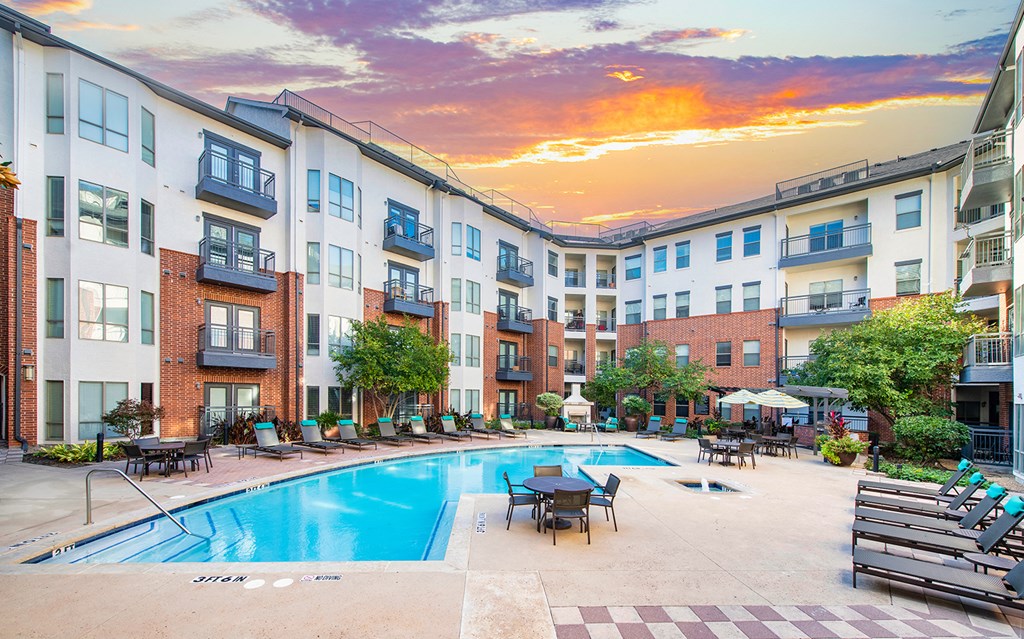 an outdoor pool with tables and chairs near an apartment building