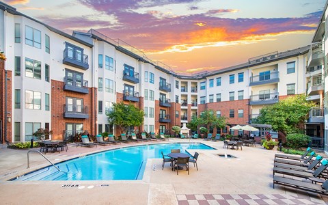 an outdoor pool with tables and chairs near an apartment building