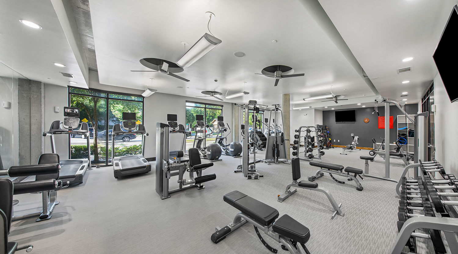 a gym with weights and cardio equipment in a building with windows