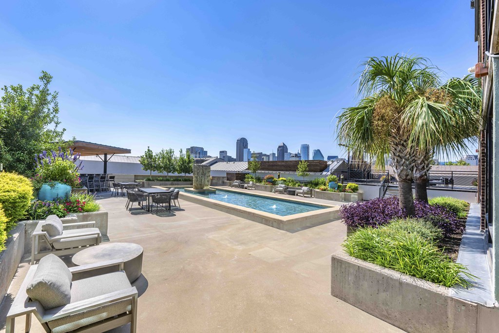 A patio with a table and chairs overlooks a pool and a city skyline.