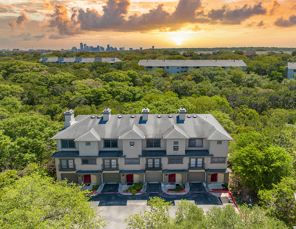 a large house surrounded by trees with a sunset in the sky