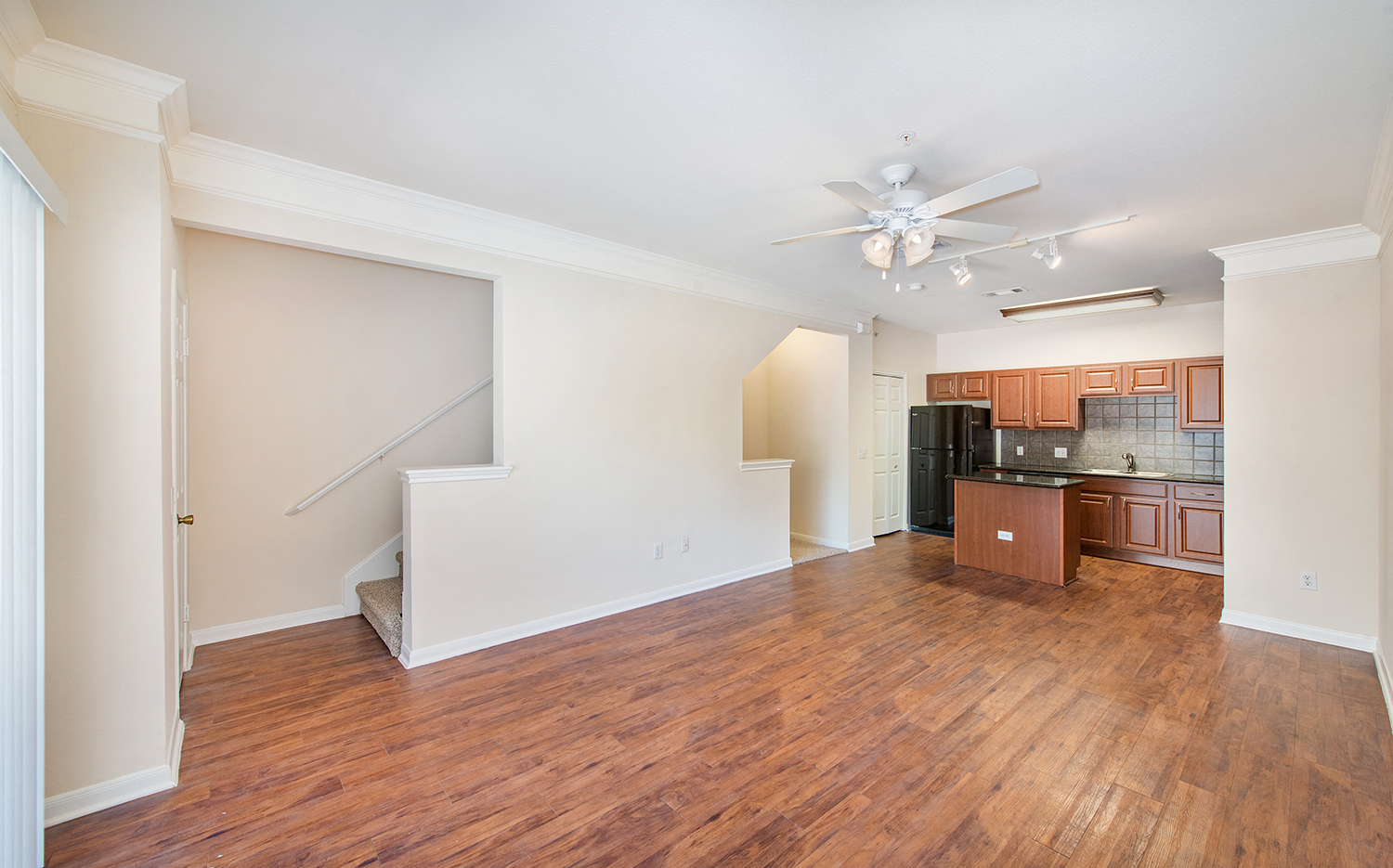 an empty living room and kitchen with wood flooring and a ceiling fan