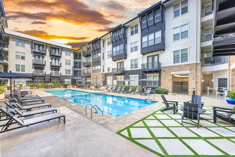 A sunset view of a pool area with lounge chairs and a green and white patterned rug.