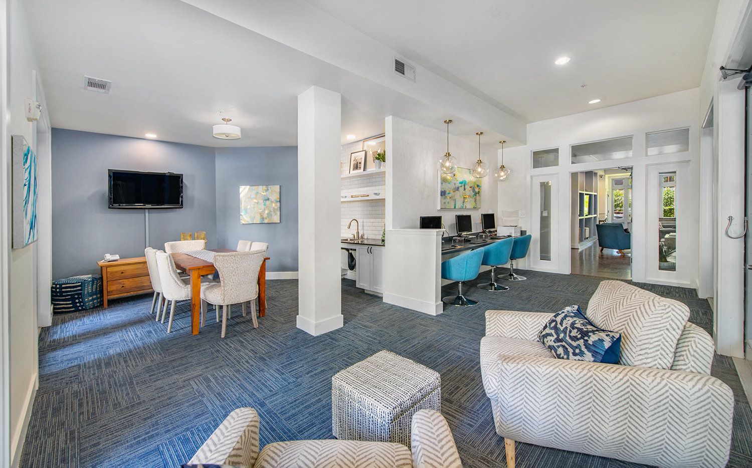 a living room with blue carpet and furniture and a kitchen with a table and chairs