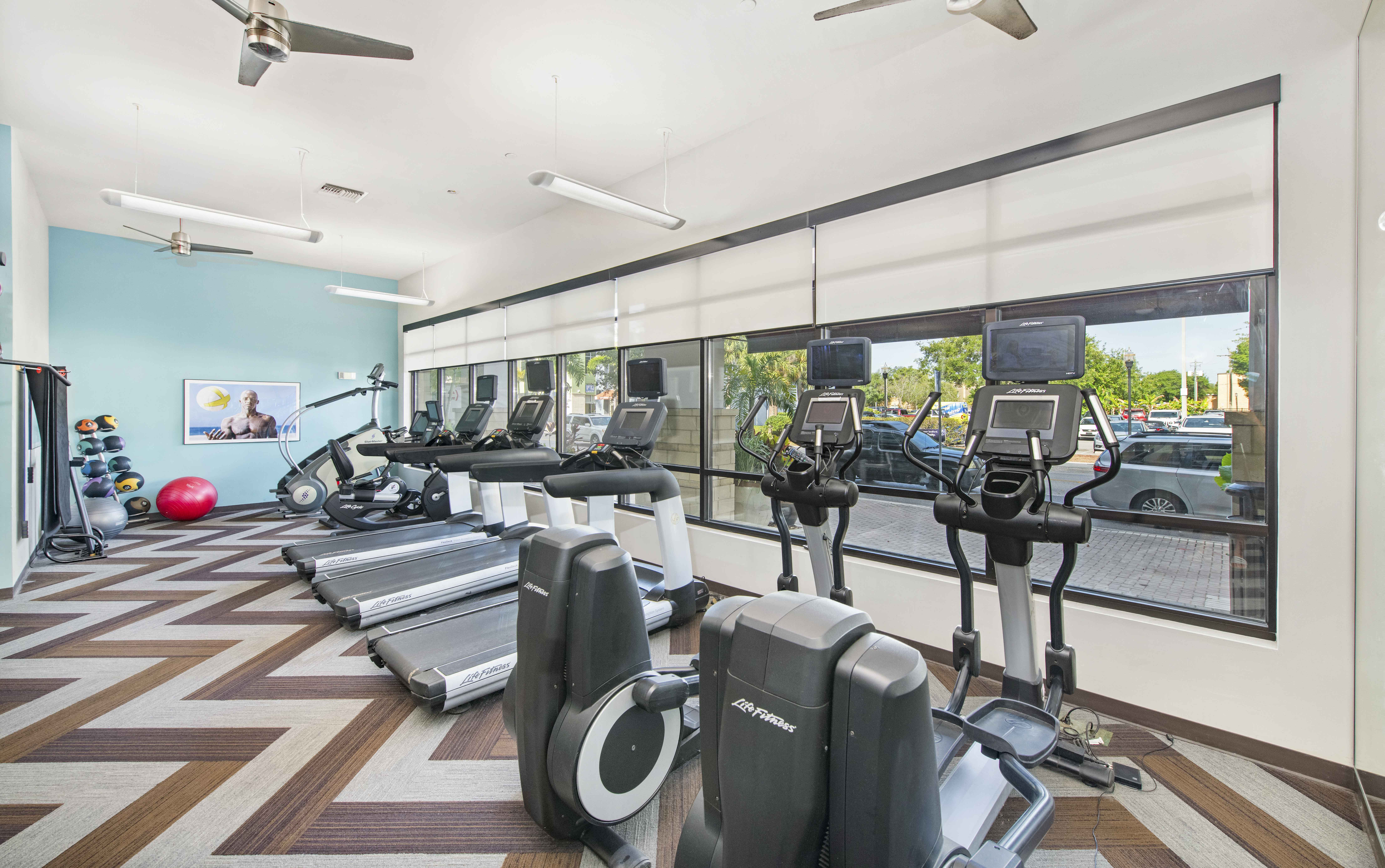 a gym with cardio machines and windows at the district flats apartments in lenexa