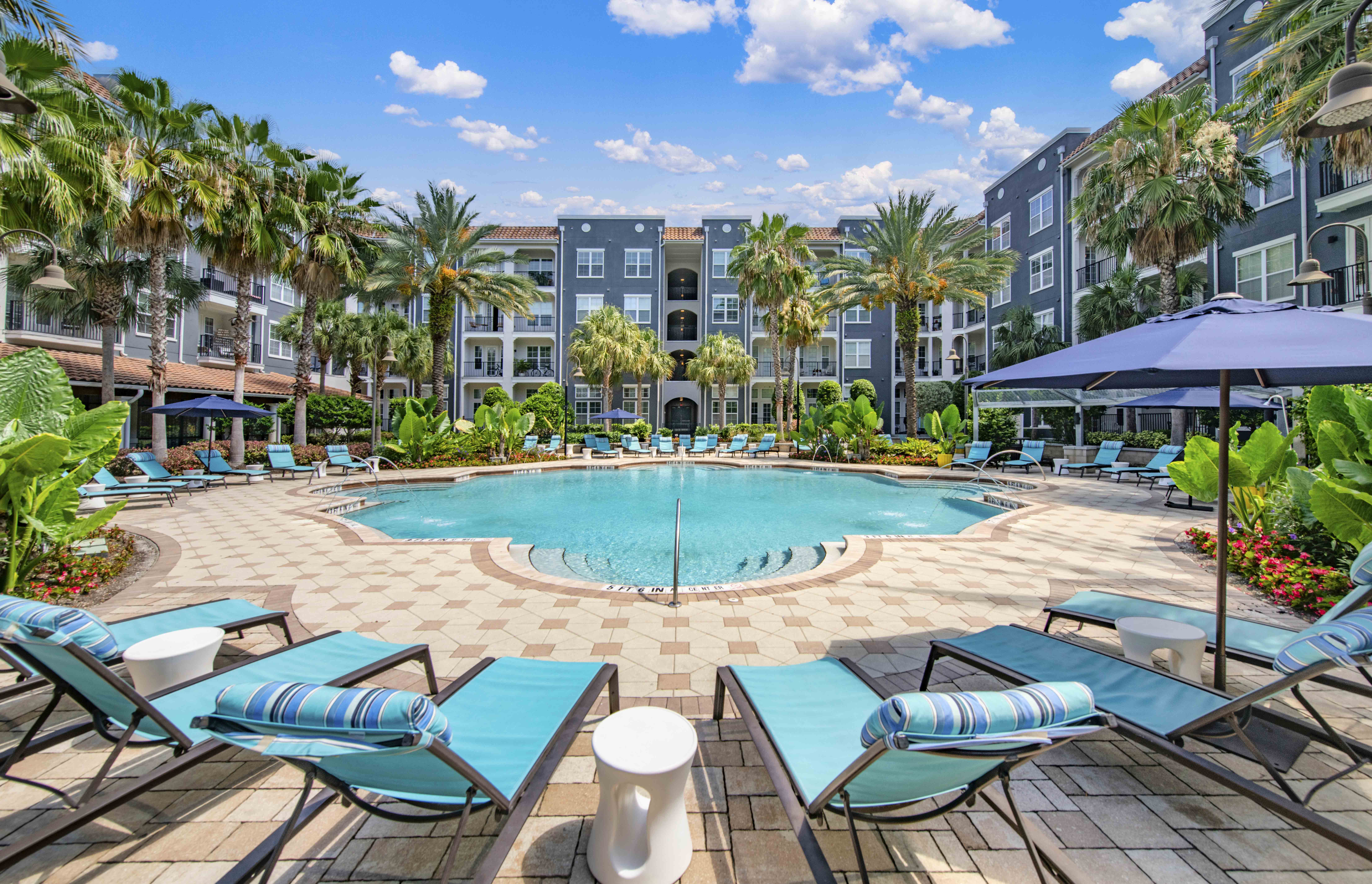 a swimming pool with lounge chairs and umbrellas in front of an apartment building