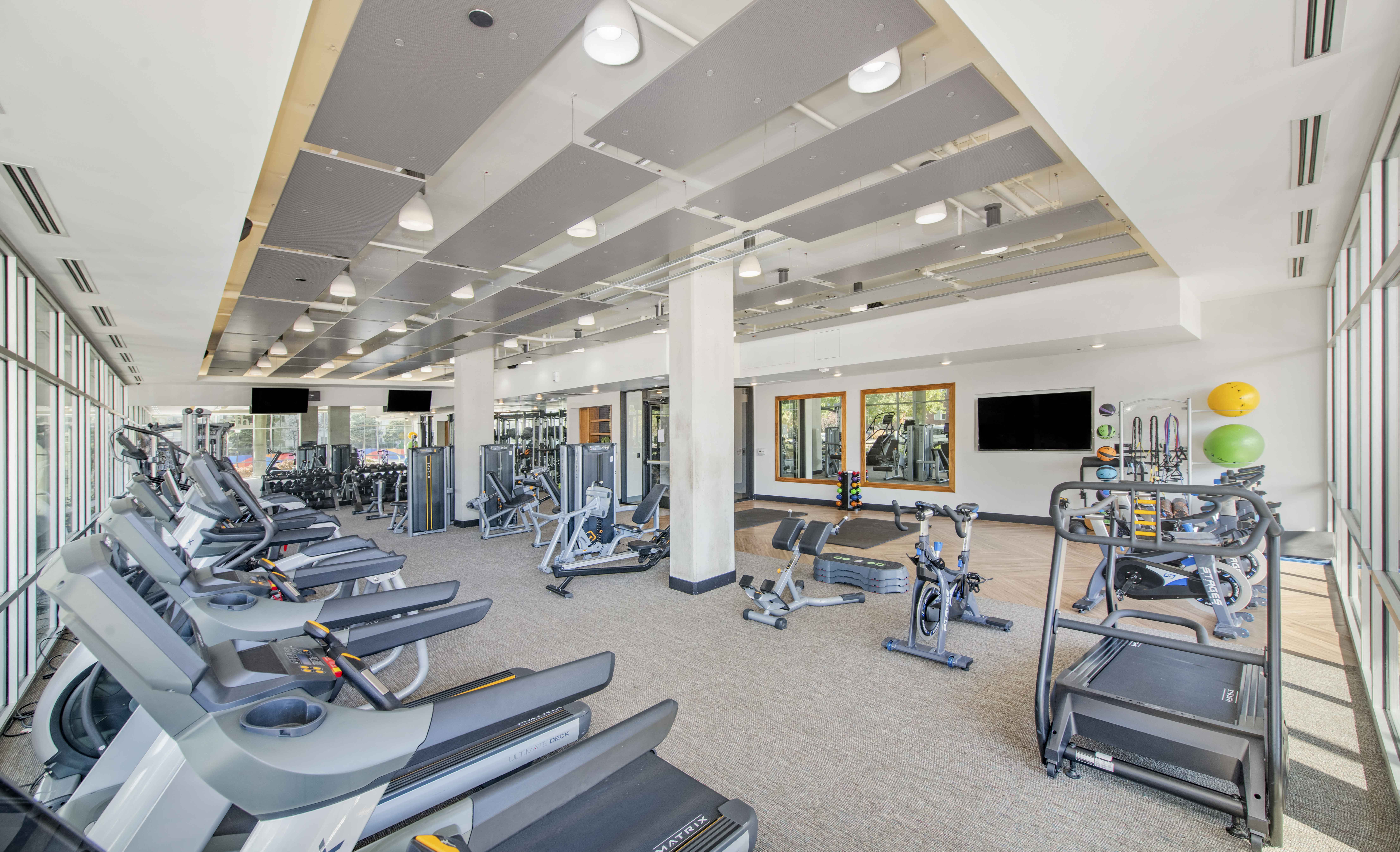 a gym with cardio equipment and weights in a building with windows
