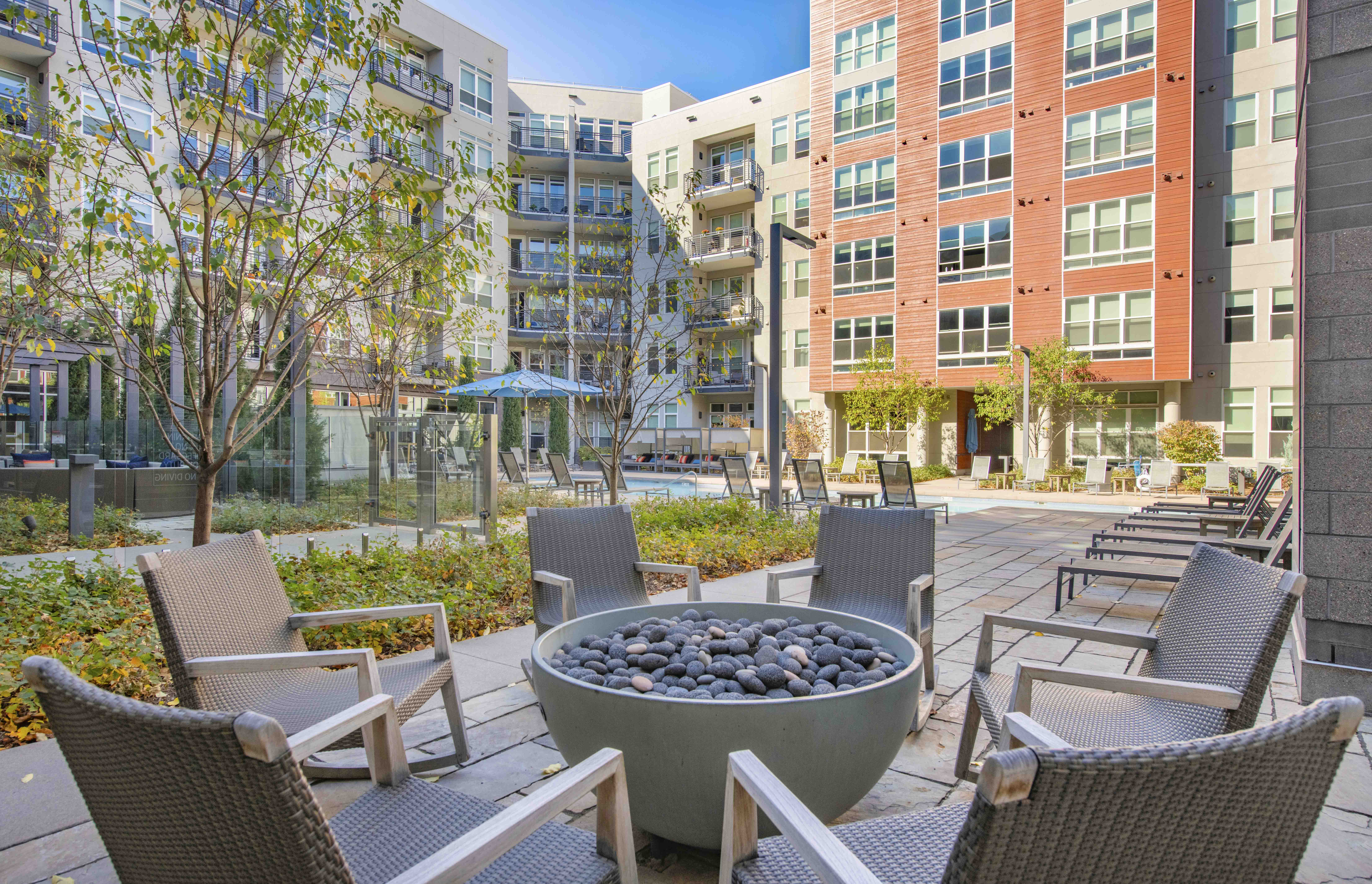 an outdoor patio with chairs and a fire pit in front of an apartment building