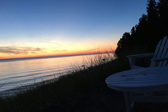 a sunset over the water with two chairs on the shore