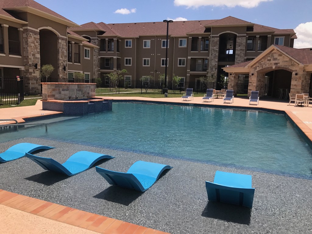 a large swimming pool with blue chairs in front of an apartment building