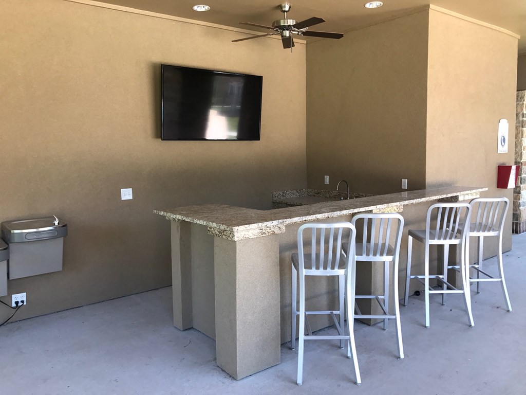 a bar area with stools and a tv in the wall