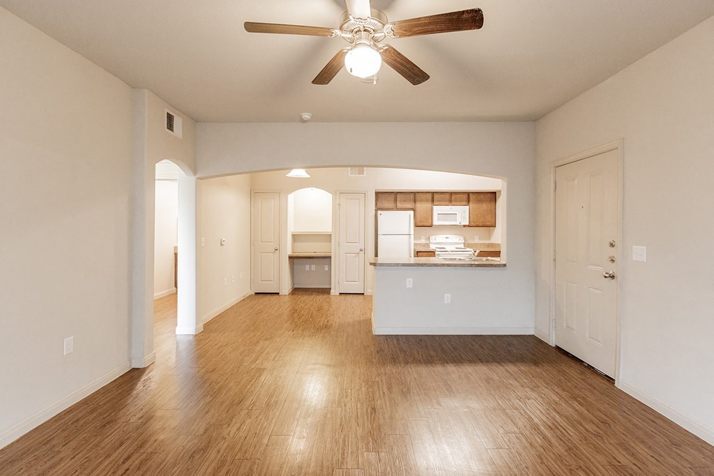 an empty living room with a ceiling fan and a kitchen