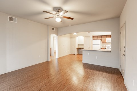 an empty living room with a ceiling fan and a kitchen