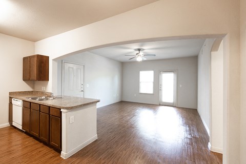 an empty living room with a kitchen and a ceiling fan