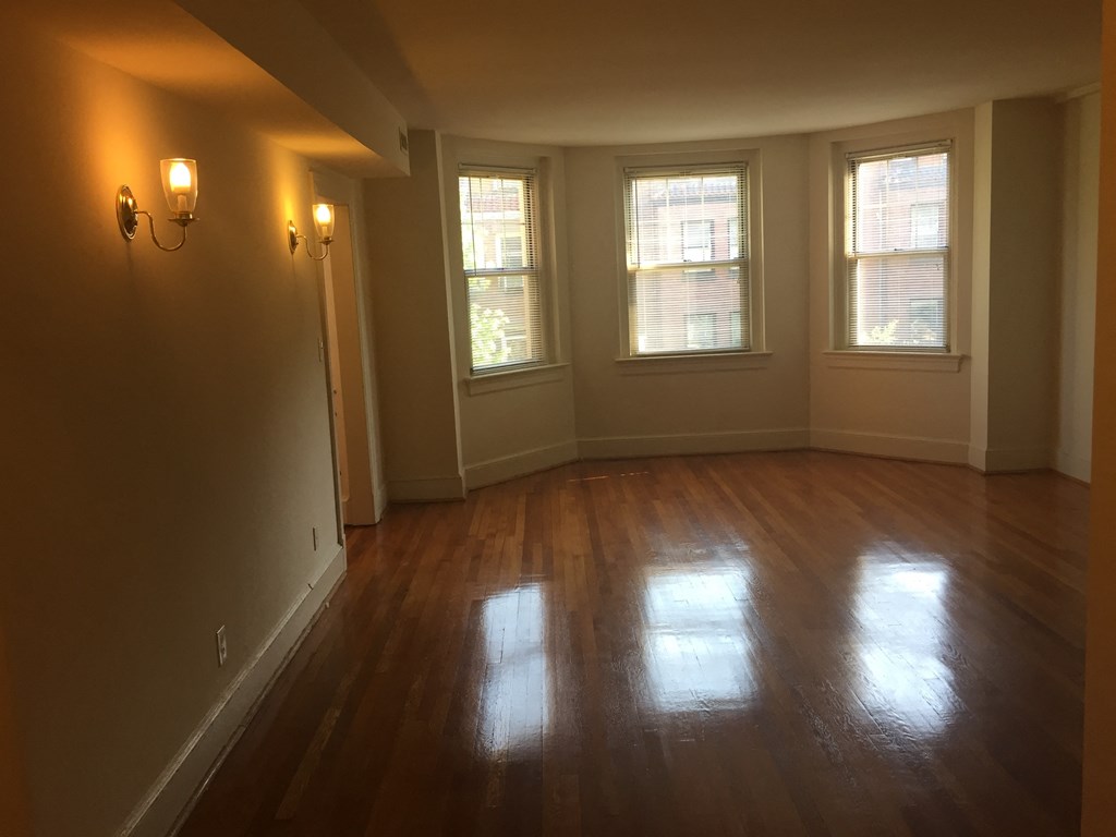 an empty living room with wooden floors and three windows