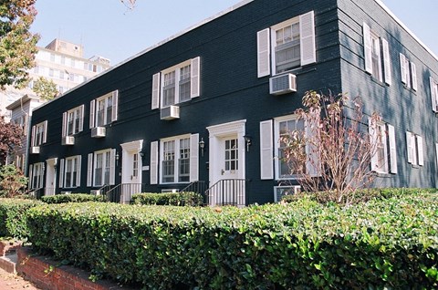 a black house with white windows and a hedge in front of it
