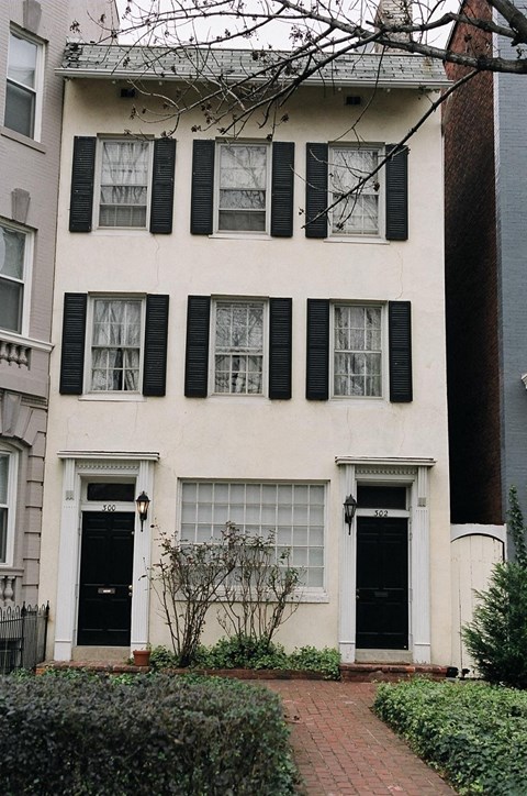 a white house with black shuttered windows and a sidewalk