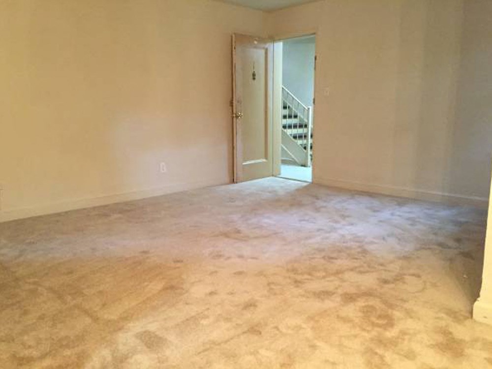 an empty living room with the door open to a staircase