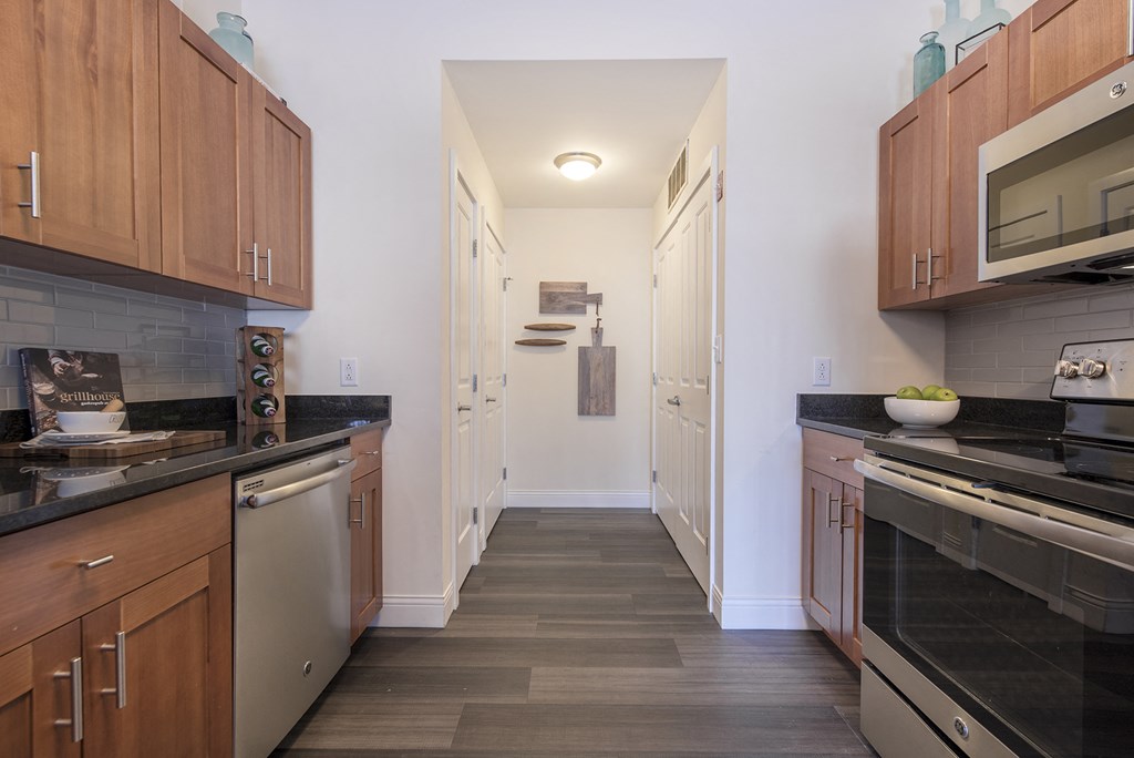 a kitchen with wooden cabinets and black counter tops and a long hallway