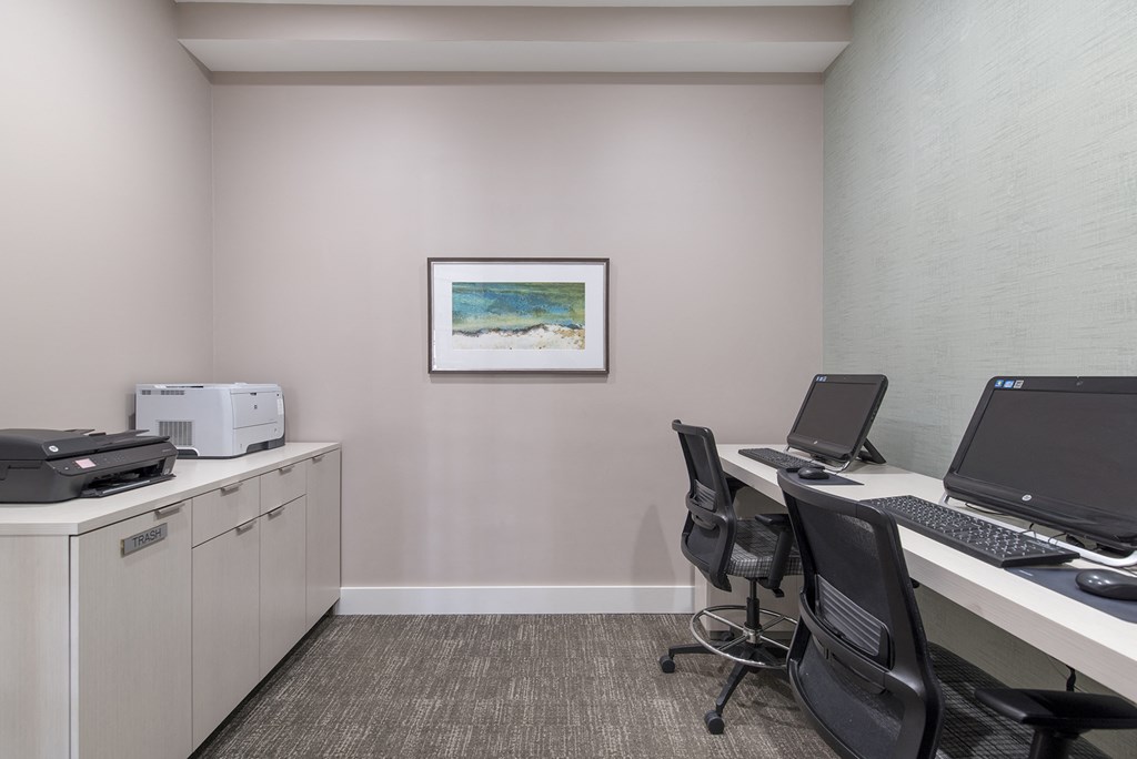 an office with two desks with computers and a printer and a painting on the wall