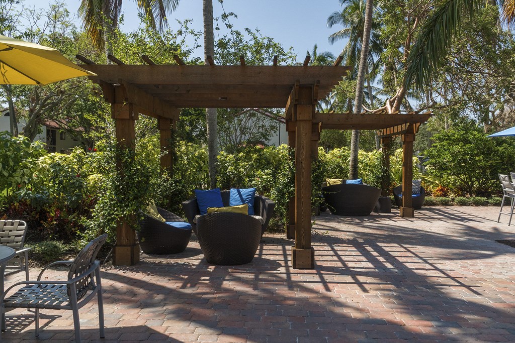 a pergola on a brick patio with chairs and umbrellas