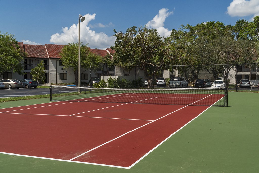 a tennis court with cars parked in front of apartment buildings