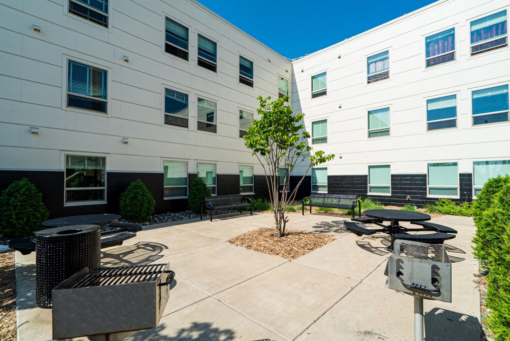 an outside patio area with tables and benches in front of a white building