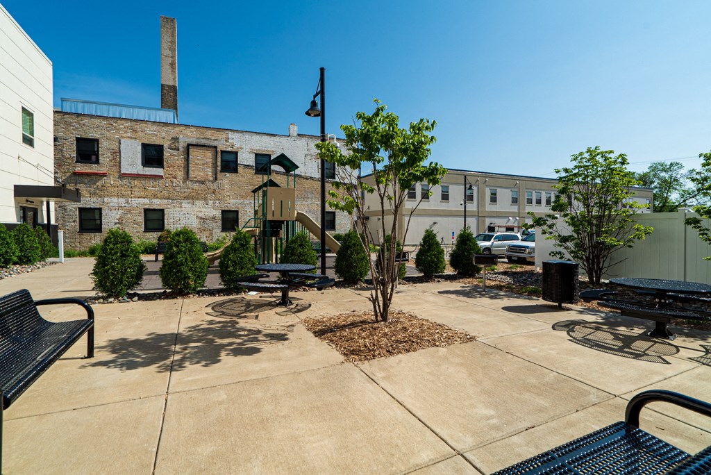 a courtyard with benches and trees in front of a brick building