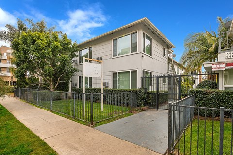 an apartment building with a sidewalk and a fence in front of it