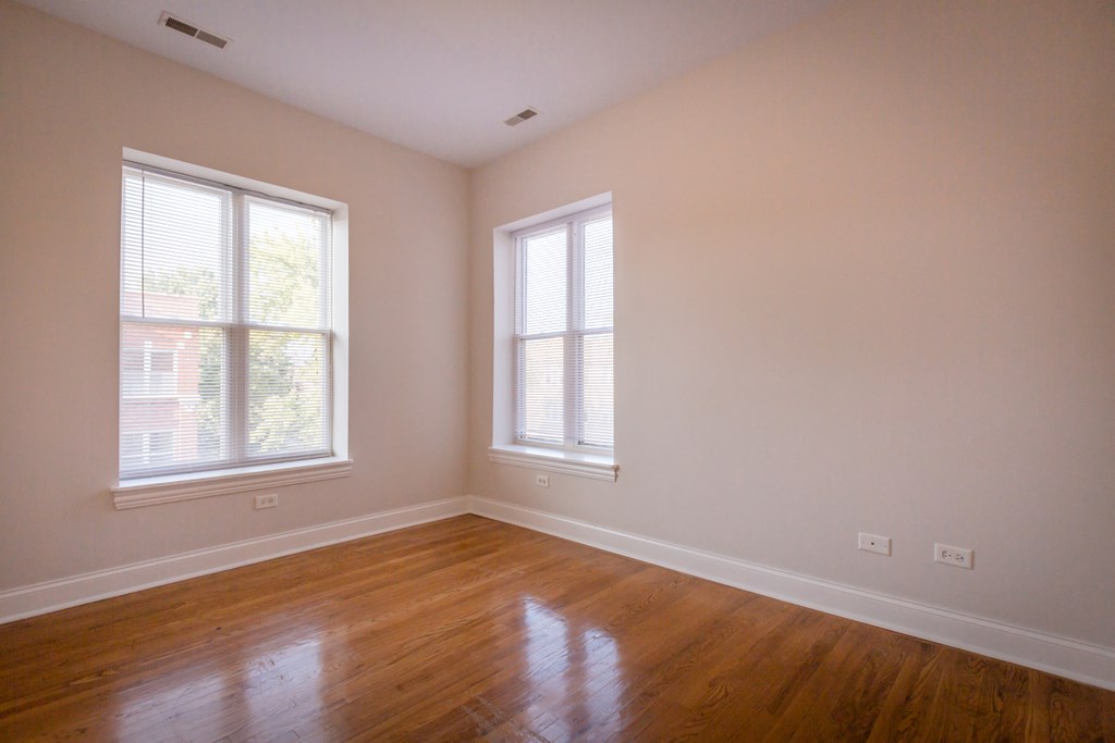an empty room with wooden floors and two windows
