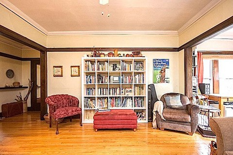 A living room with a bookshelf, a red chair, a grey armchair, and a red ottoman.