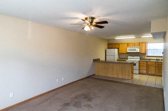an empty living room and kitchen with a ceiling fan