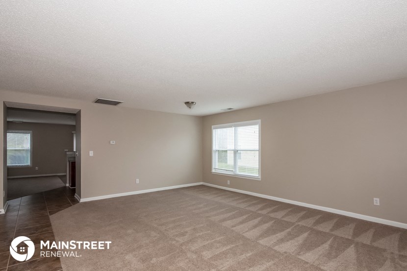 the spacious living room of this manufactured home has carpeting and a large window