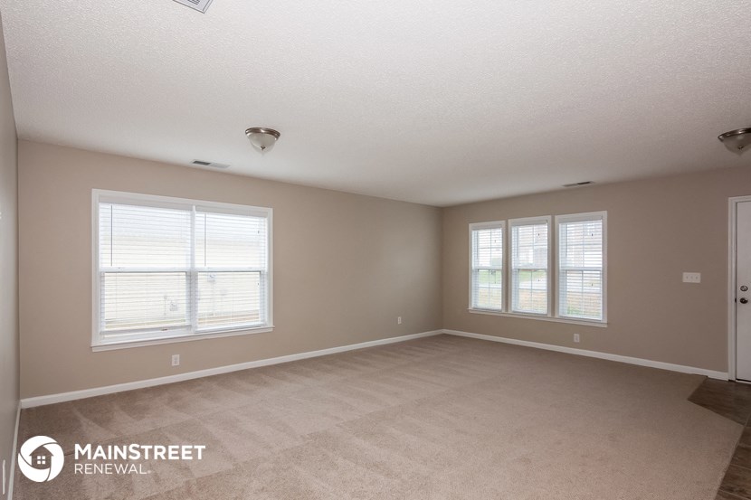 the living room of an apartment with a carpeted floor and two windows