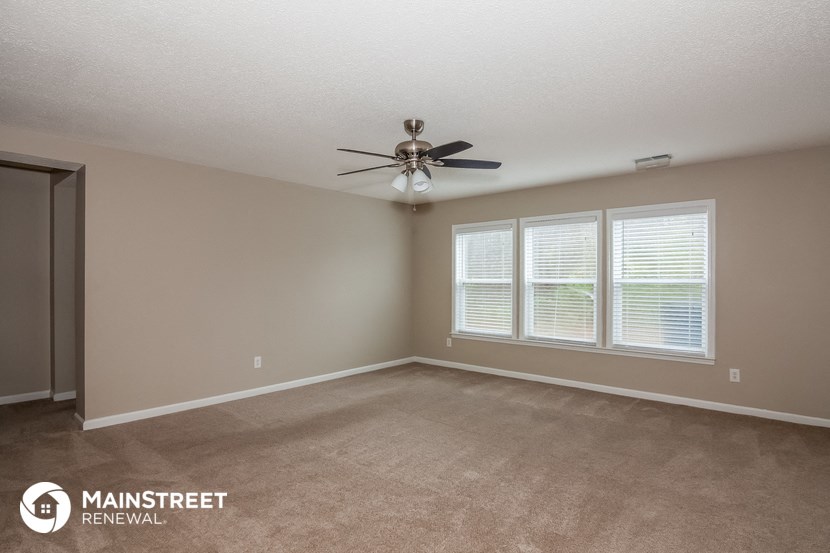 the spacious living room with ceiling fan and windows