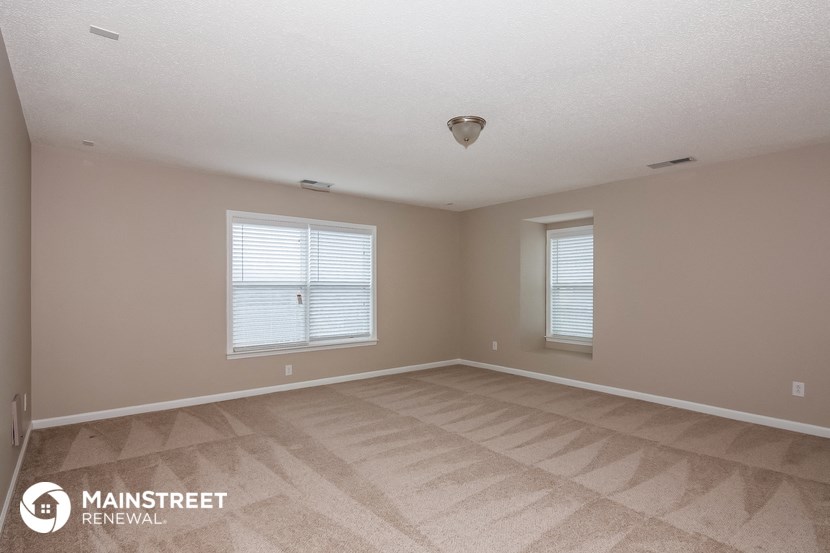 the spacious living room of a house with carpet and two windows