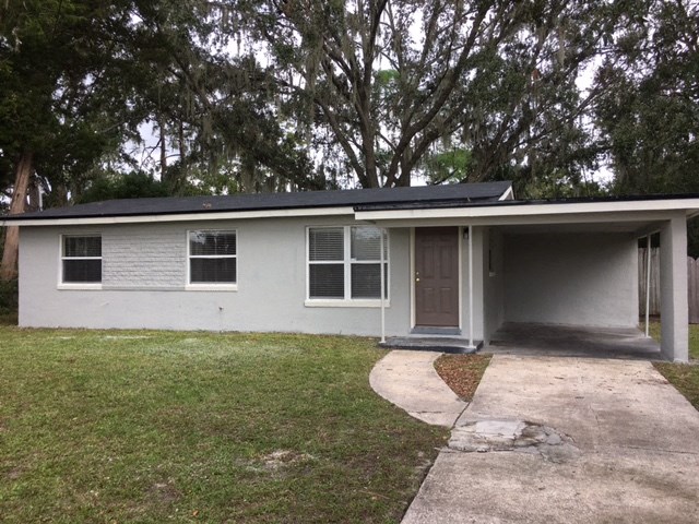 the front of a white house with a driveway and trees