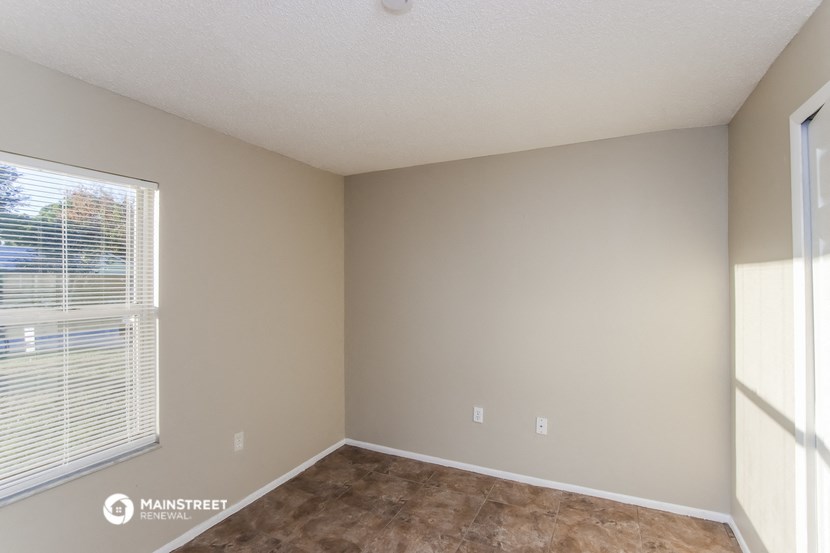 an empty room with a large window and brown flooring