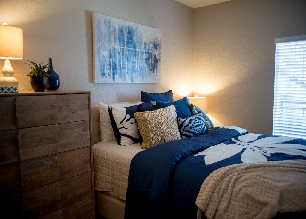 a bedroom with a bed with blue and white pillows and a dresser