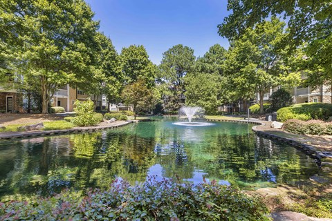 A serene pond surrounded by lush greenery and a fountain in the middle.