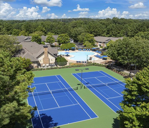 A tennis court surrounded by trees and a pool.
