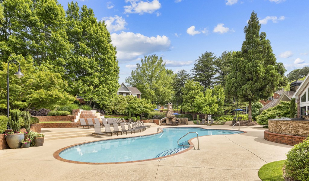 a swimming pool with chaise lounge chairs near trees and a house