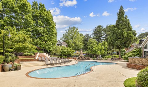 a swimming pool with chaise lounge chairs near trees and a house