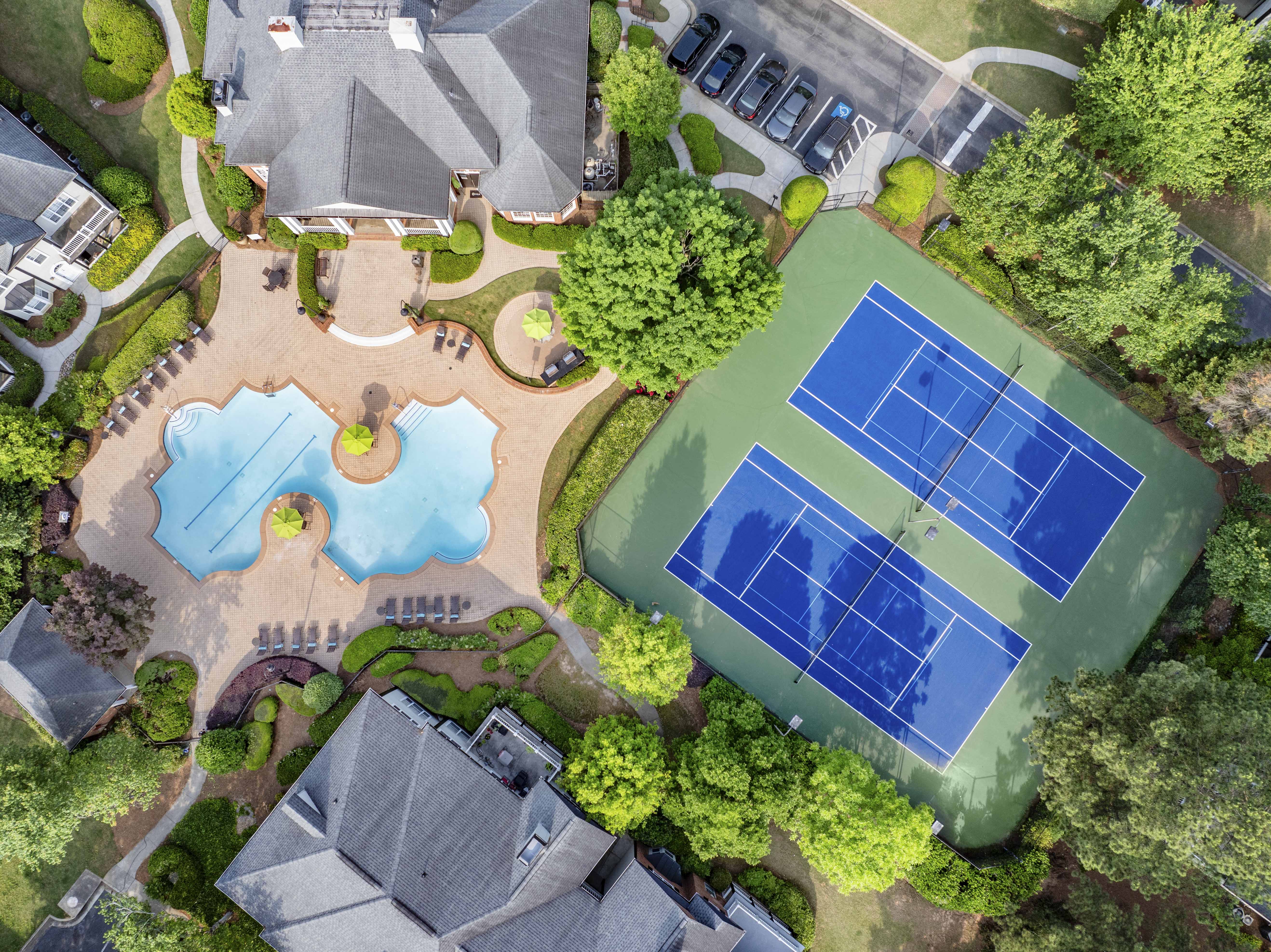 an aerial view of a tennis court and pool in a backyard with trees