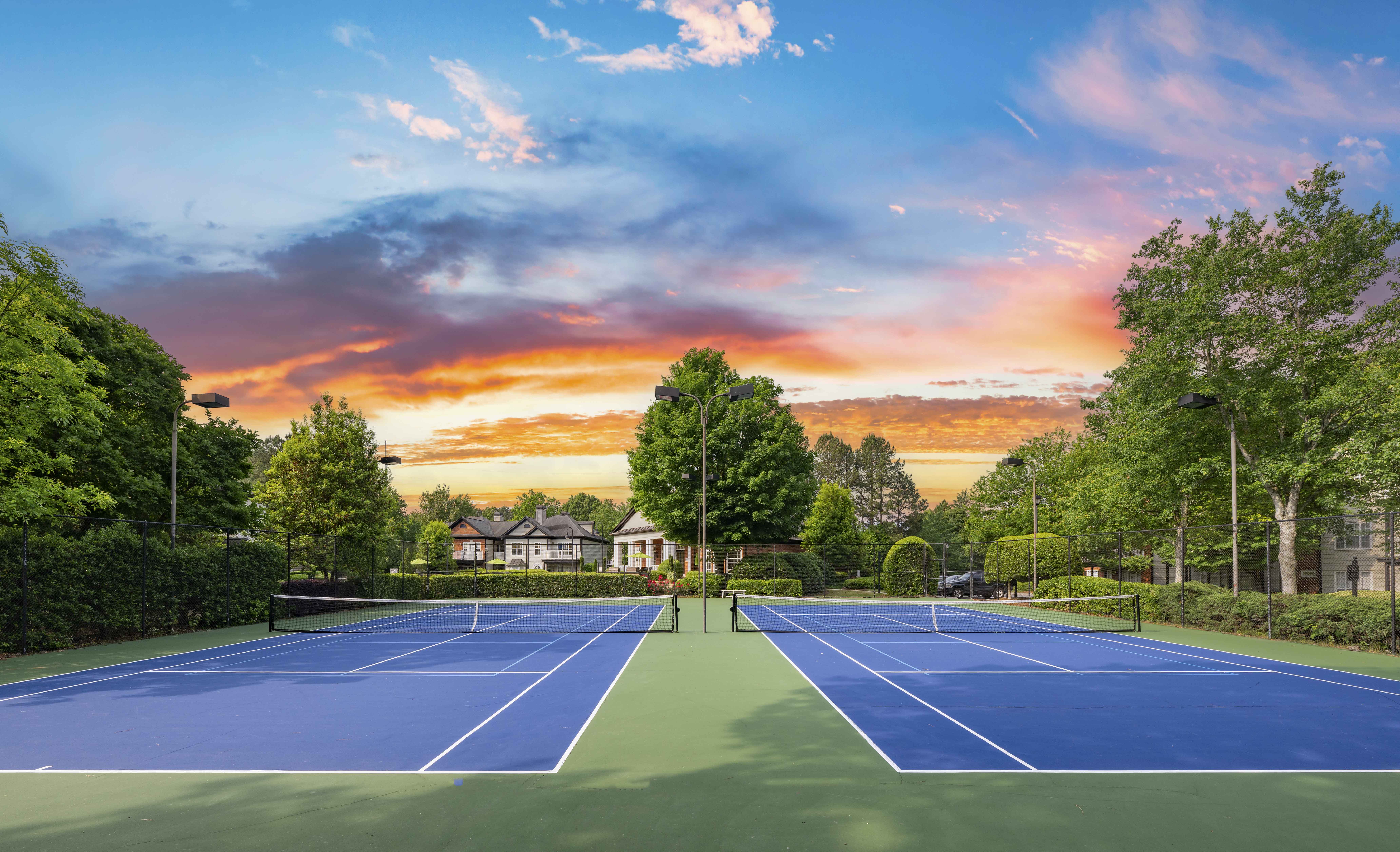 a tennis court with trees and a sunset in the background