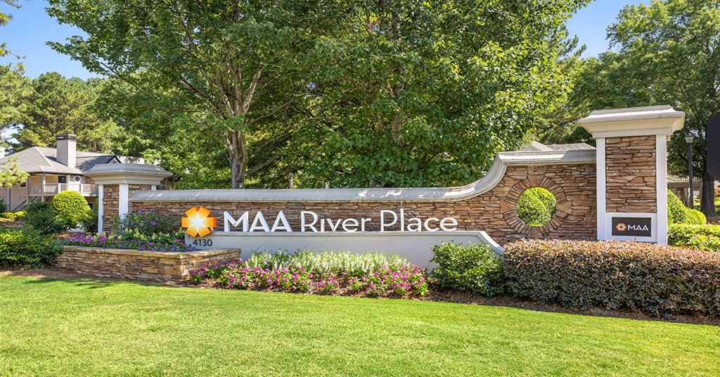 a sign for the mia river place on a stone wall with flowers and trees