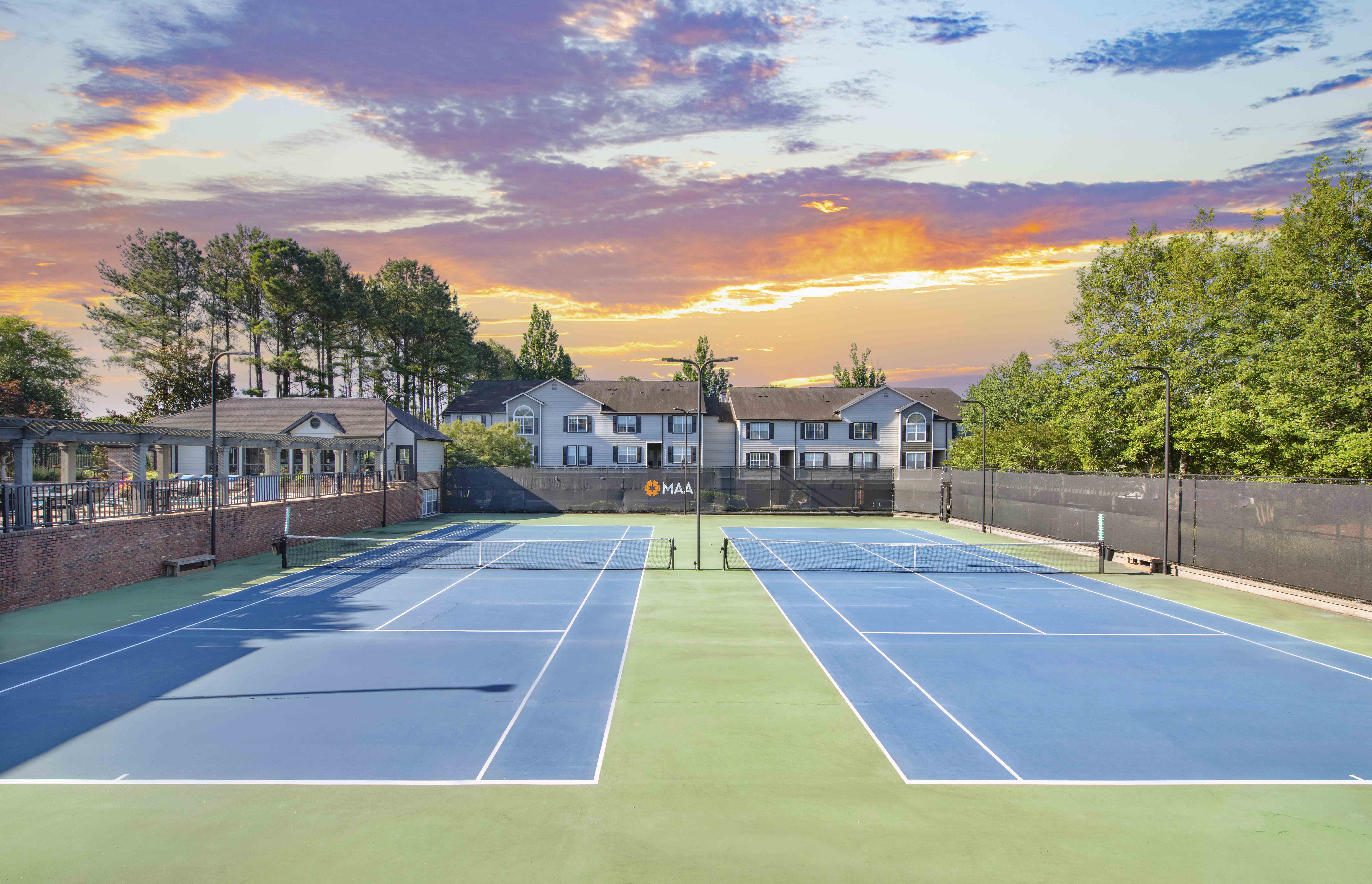 a tennis court at sunset with apartments in the background
